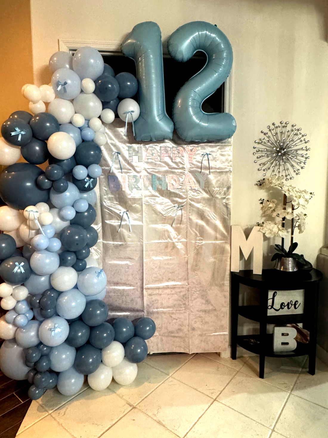 Custom 12th birthday party setup with blue balloon arch doorway, personalized decorations, and coordinated party favors including hats, gift bags, and stickers in Orlando